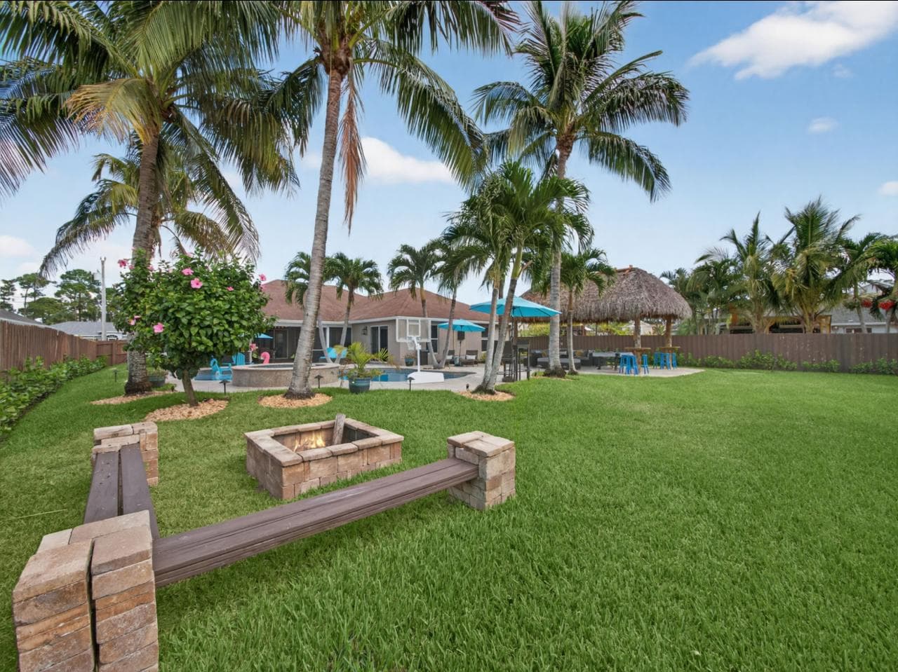 Expansive backyard with fire pit, pool, tiki hut, and palm trees